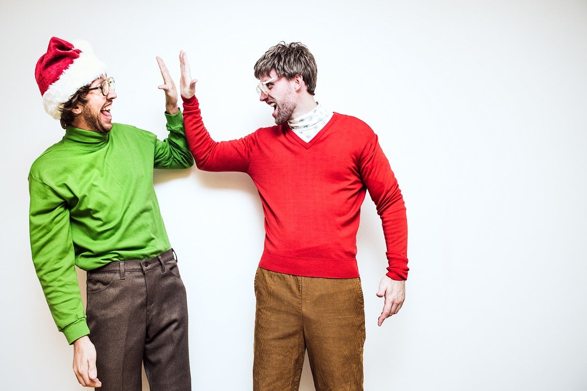 A man in a green jumper and santa hat high fiving another man wearing a red jumper