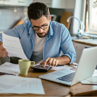 Man with documents, calculator, cup and laptop on table while working from home.