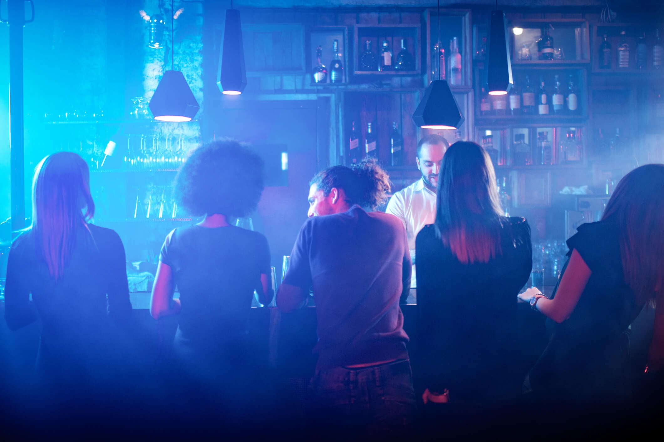 A man in a white shirt serves four customers in his bar at night time 