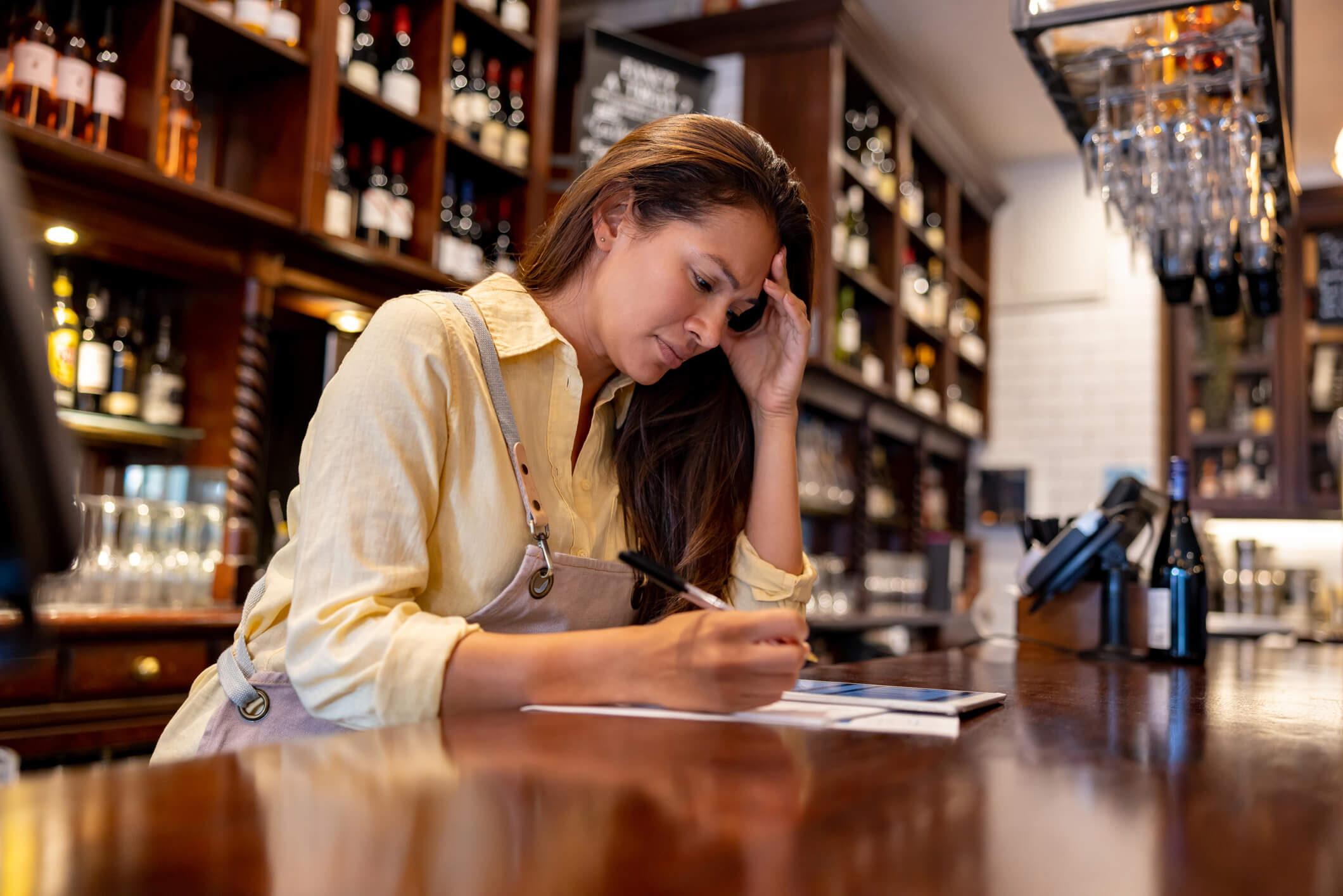 Business owner behind a bar looking frustrated managing admin on a tablet