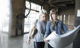 One woman holds business plans while another looks at them.