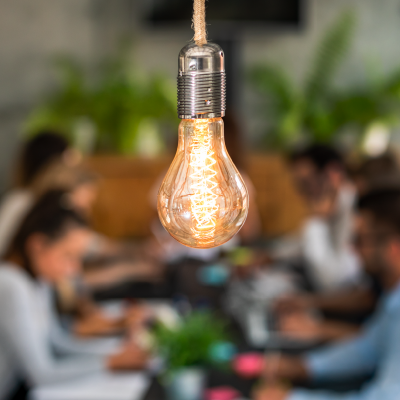 Close up of bright filament light bulb with people in office in background