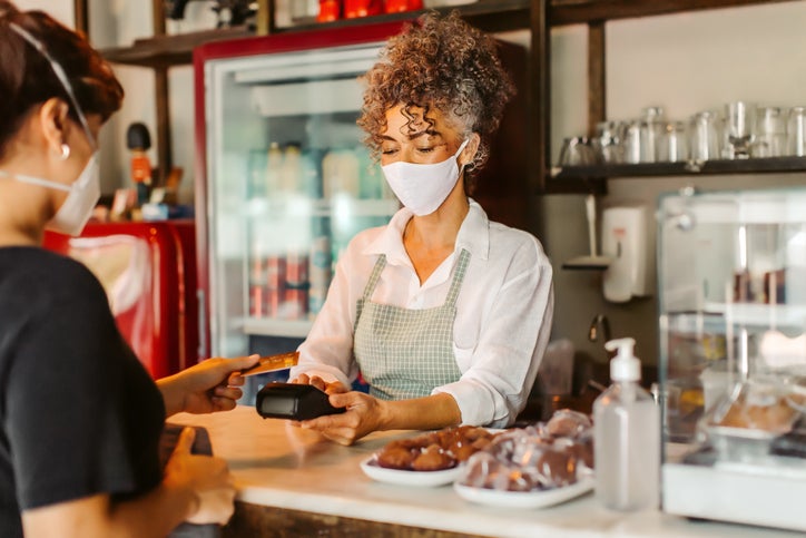 Business owner in a face mask taking a card payment from a customer. 