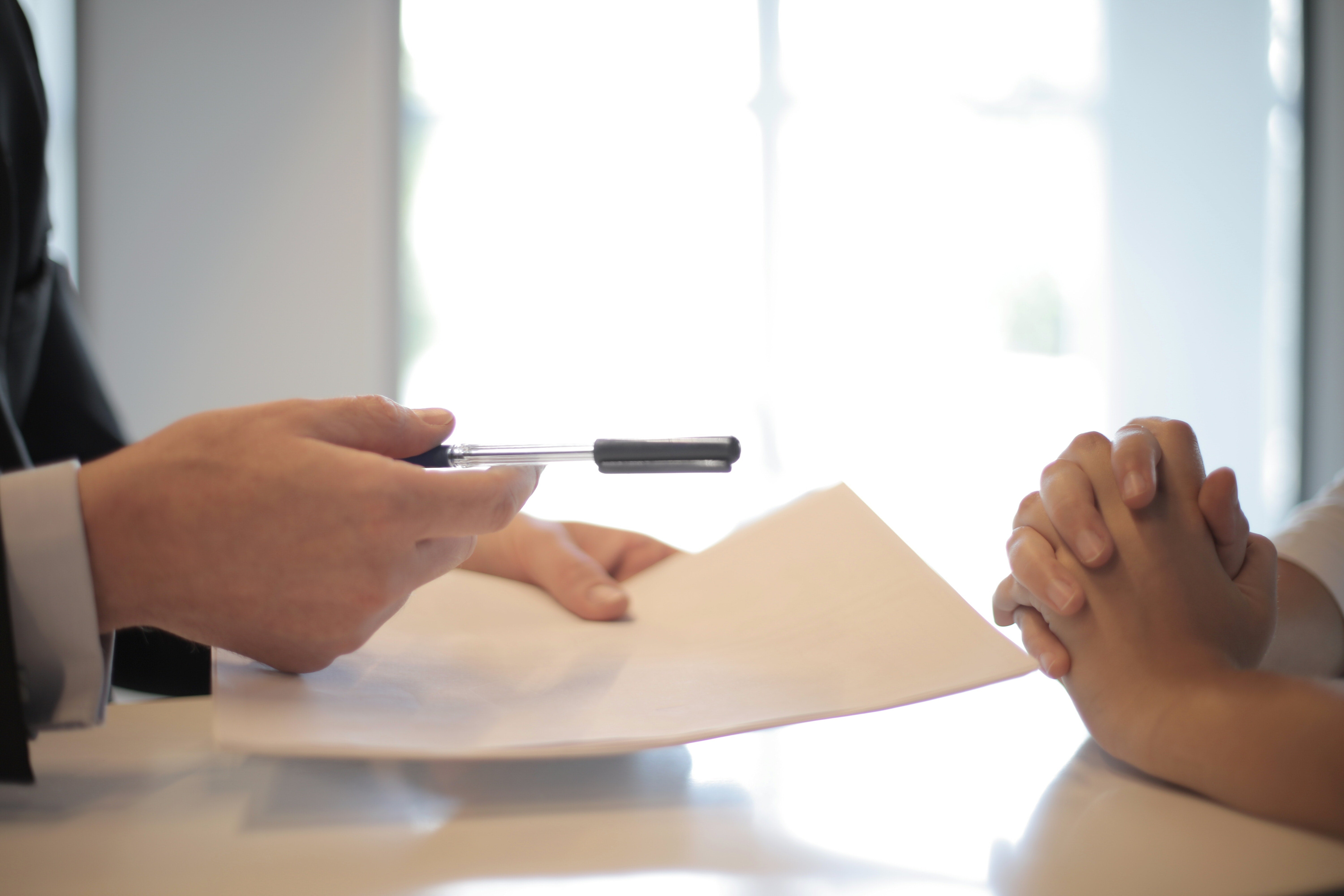 Two pairs of hands, one holding a piece of paper and a pen out to the other