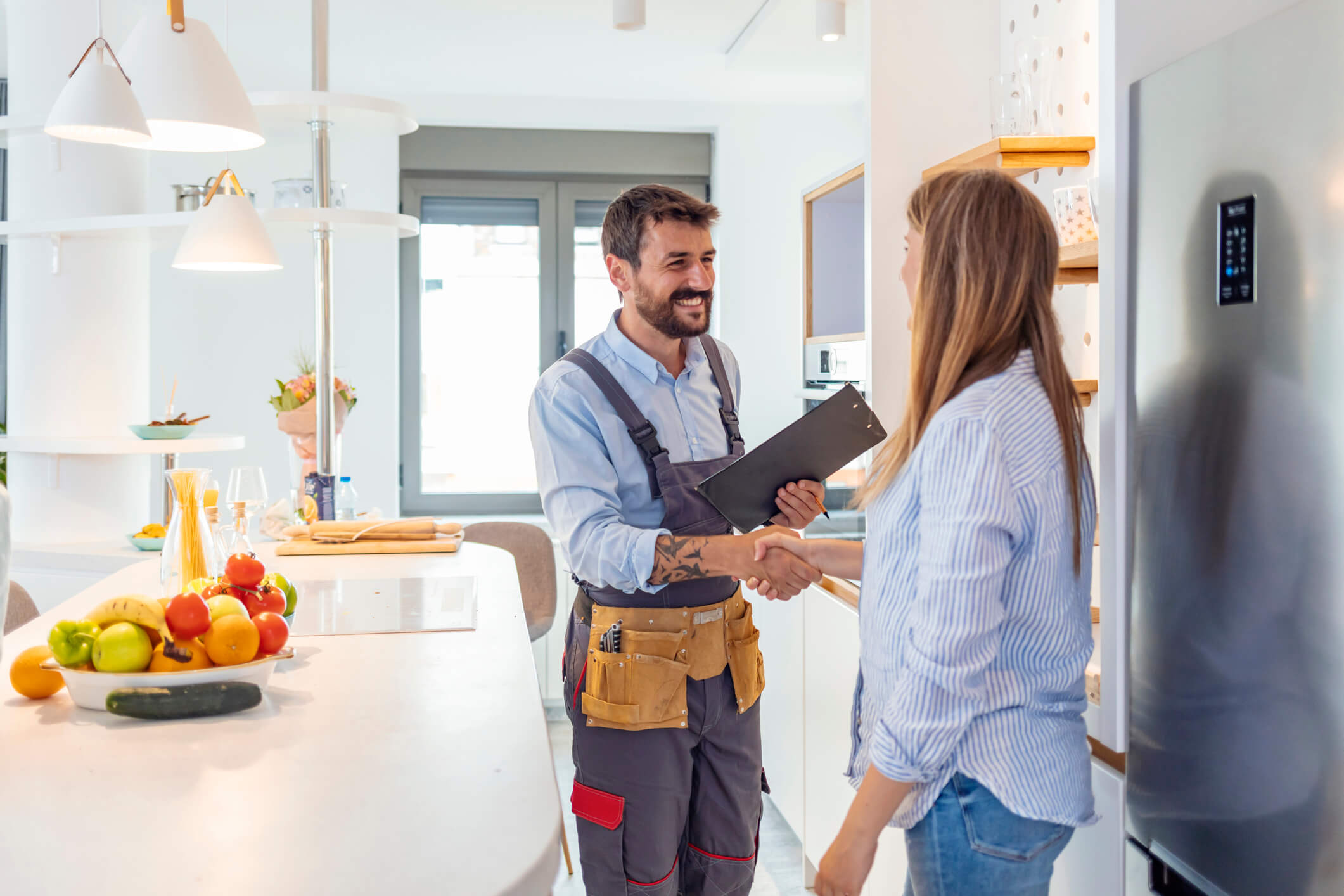 A tradesman shakes hands with a home owner in her kitchen. 