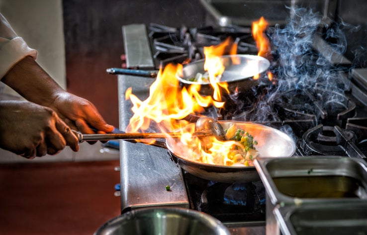 Close up of chef's hand preparing Indian food by flame in frying pan in a restaurant kitchen