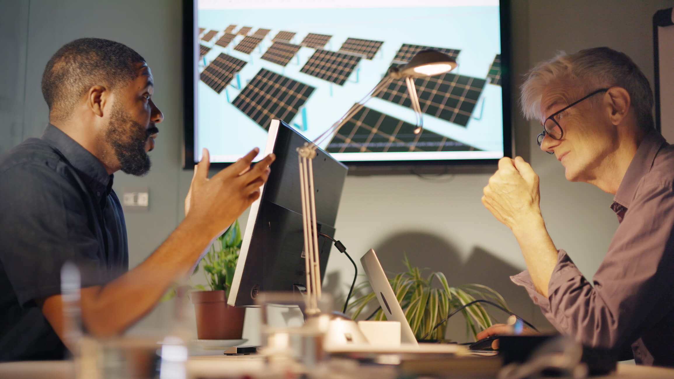 energy consultant speaking to a client at a desk with laptop and screens