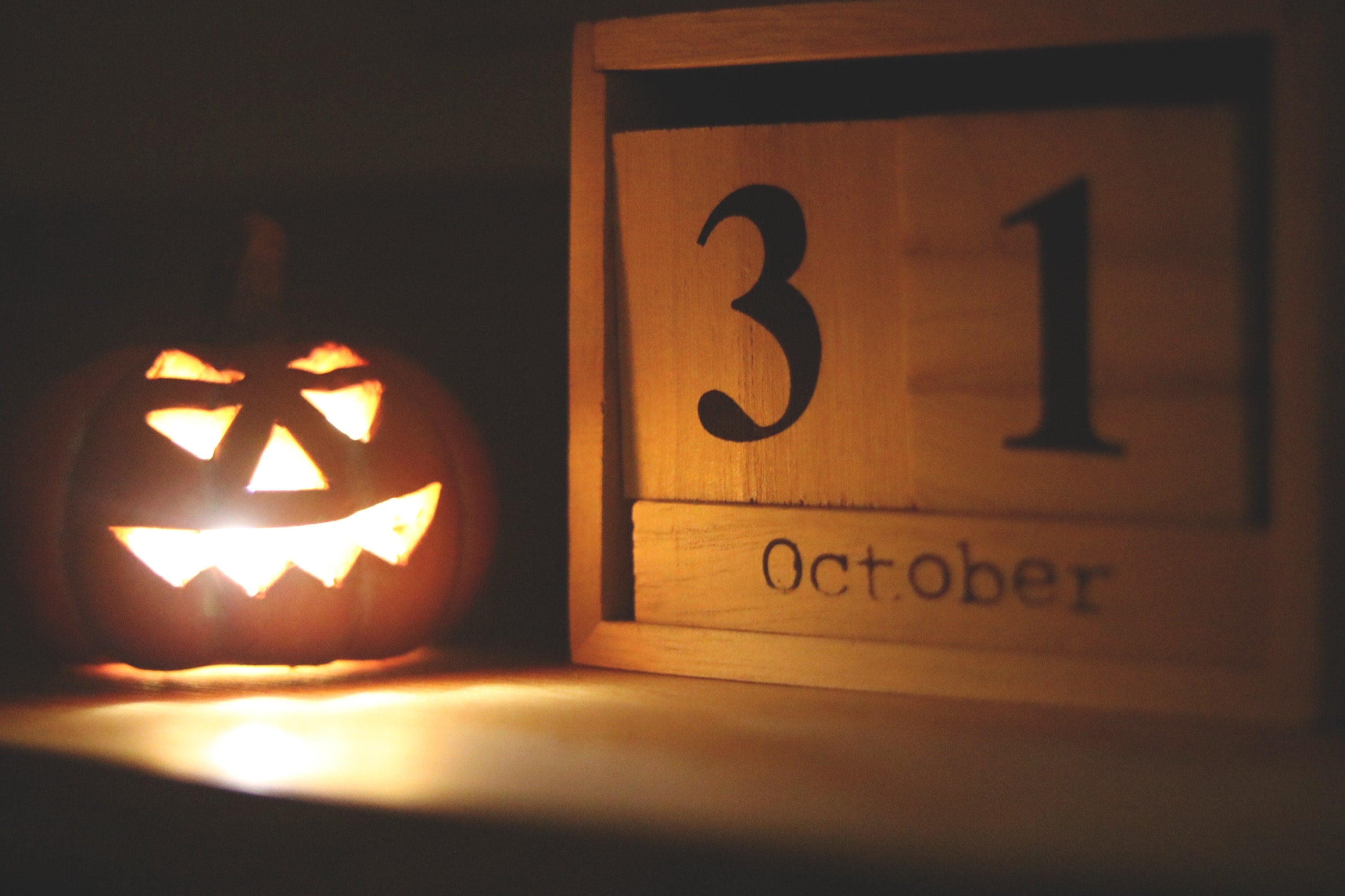 Glowing carved pumpkin next to a wooden calendar showing the date 'October 31'