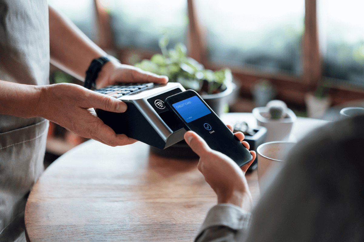 male holding a payment terminal connected to Wi-Fi with a customer using phone contactless to pay for coffee