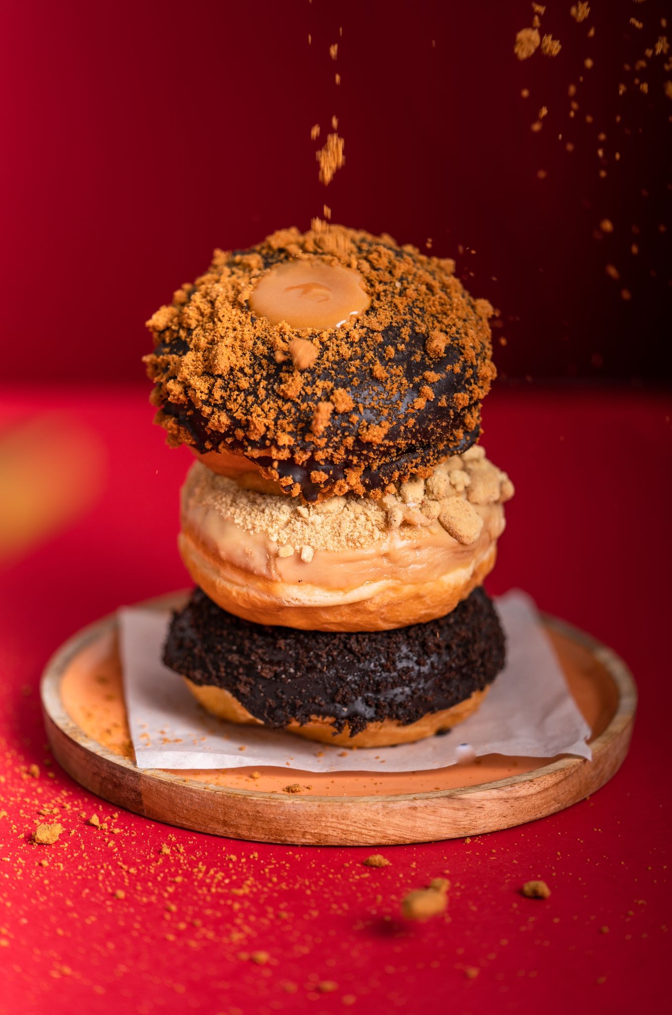 An assortment of three doughnuts sprinkled with caramel and chocolate on a red table 