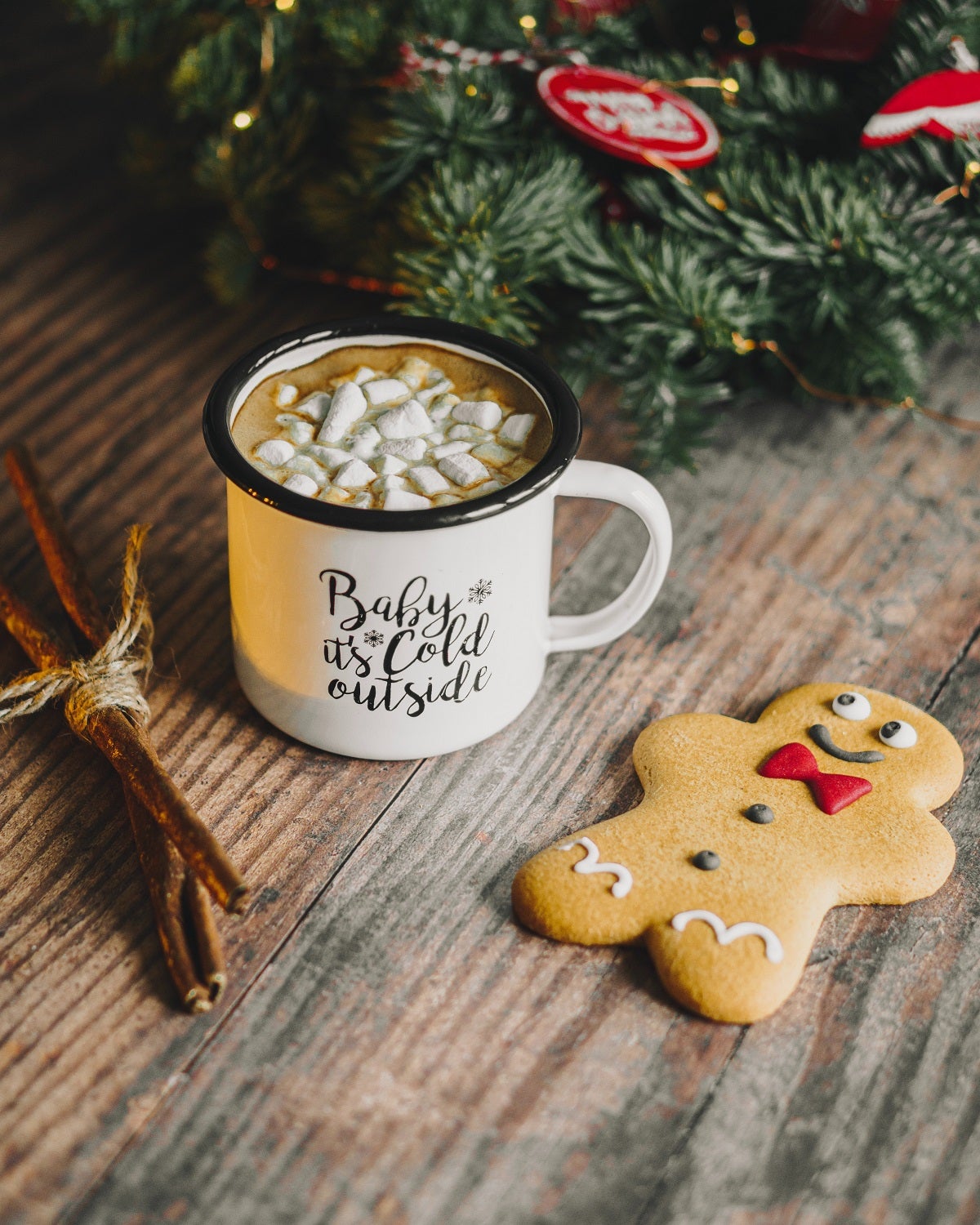 A mug of hot chocolate with marshmallows next to a smiling gingerbread man