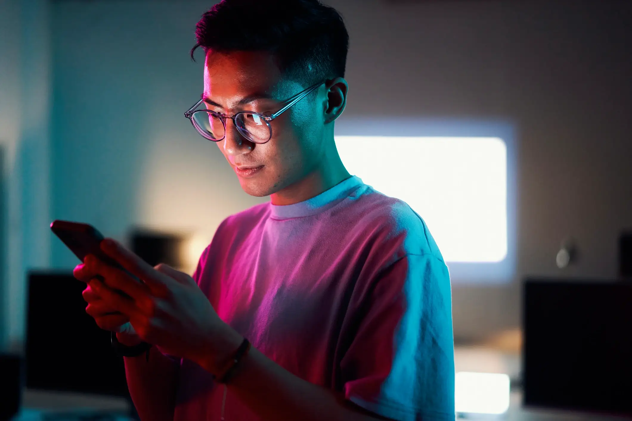 Male standing in an office in a pink light using a smartphone