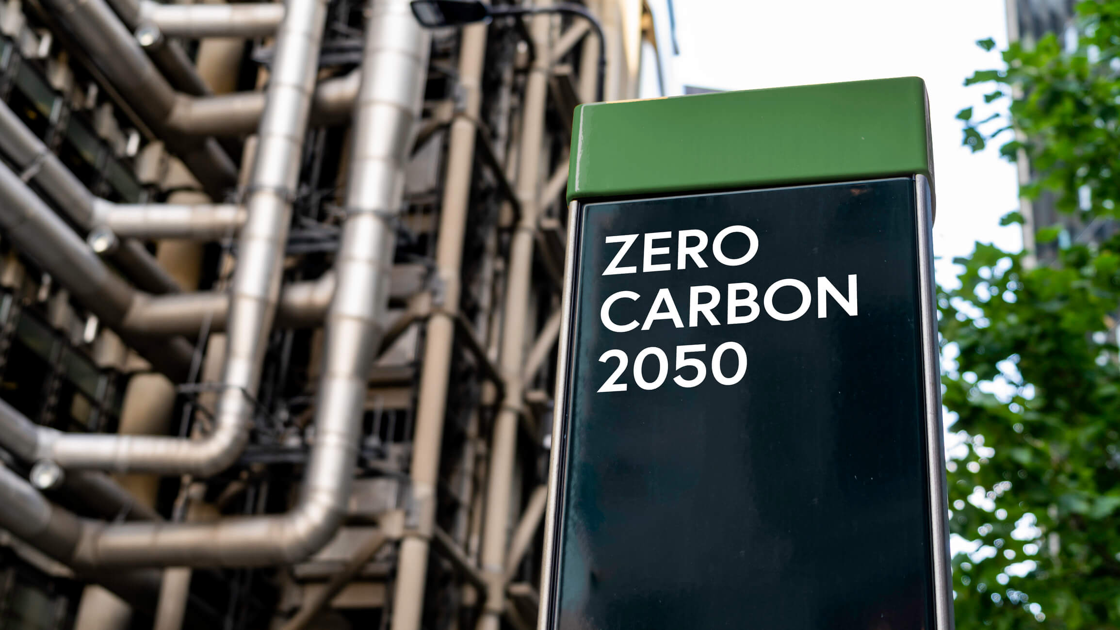 industrial pipe plant with sign in front stating zero carbon 2050
