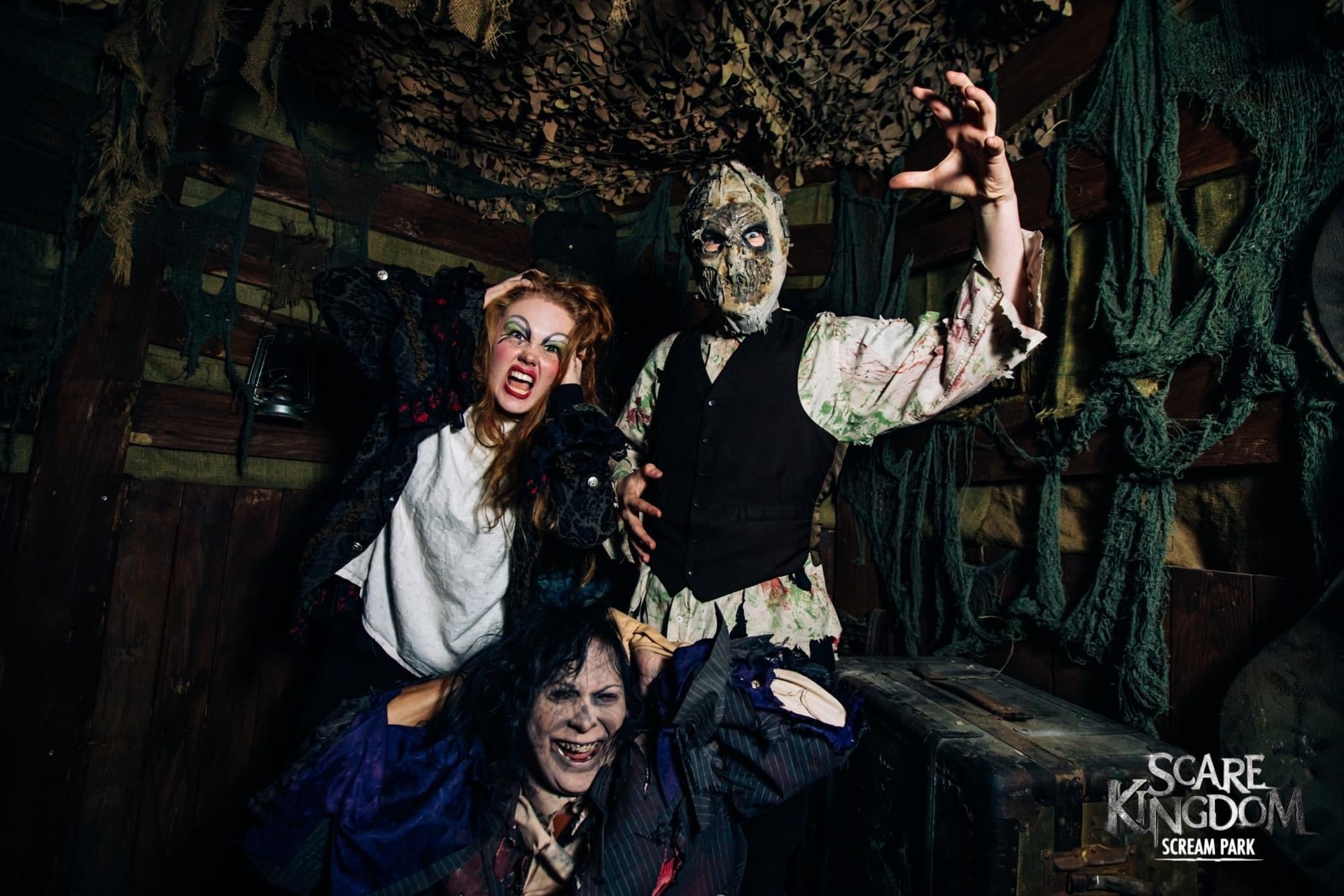 Three scare maze actors pose together with masks obscuring their faces in dark lighting 