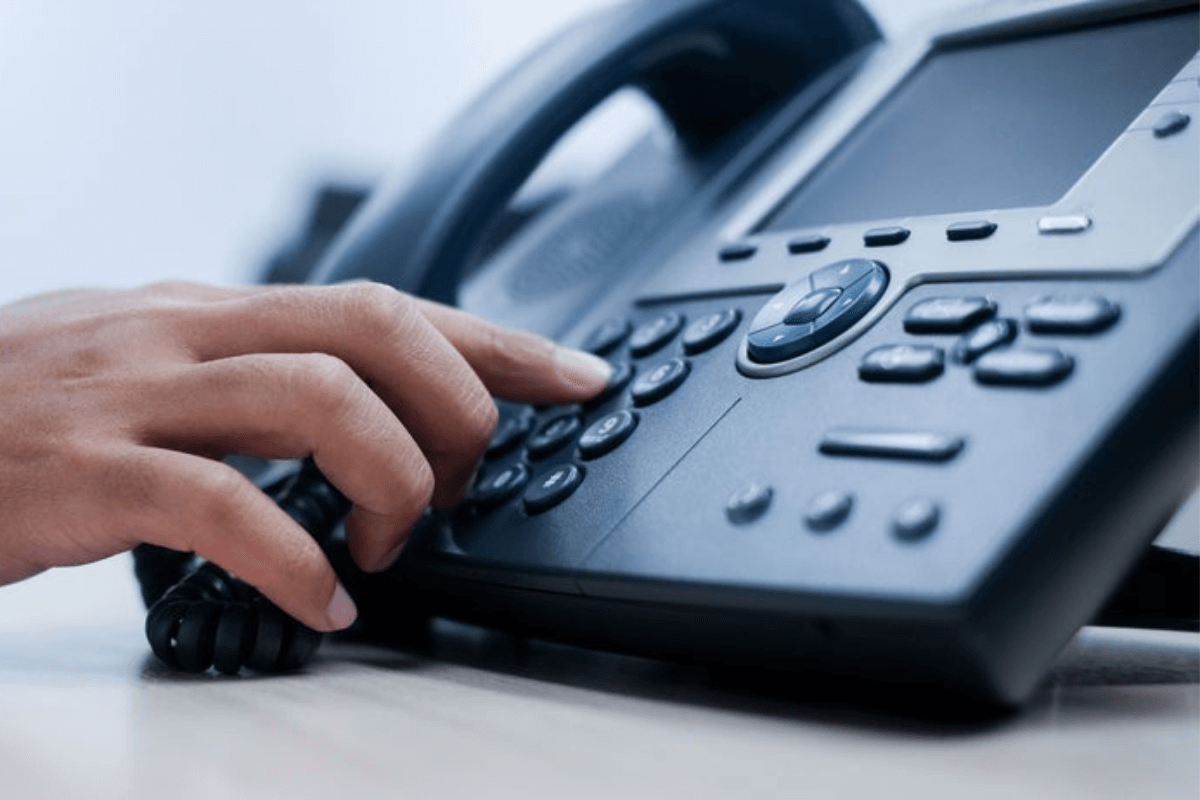 someone pressing the keys on a desk phone sitting on a desk