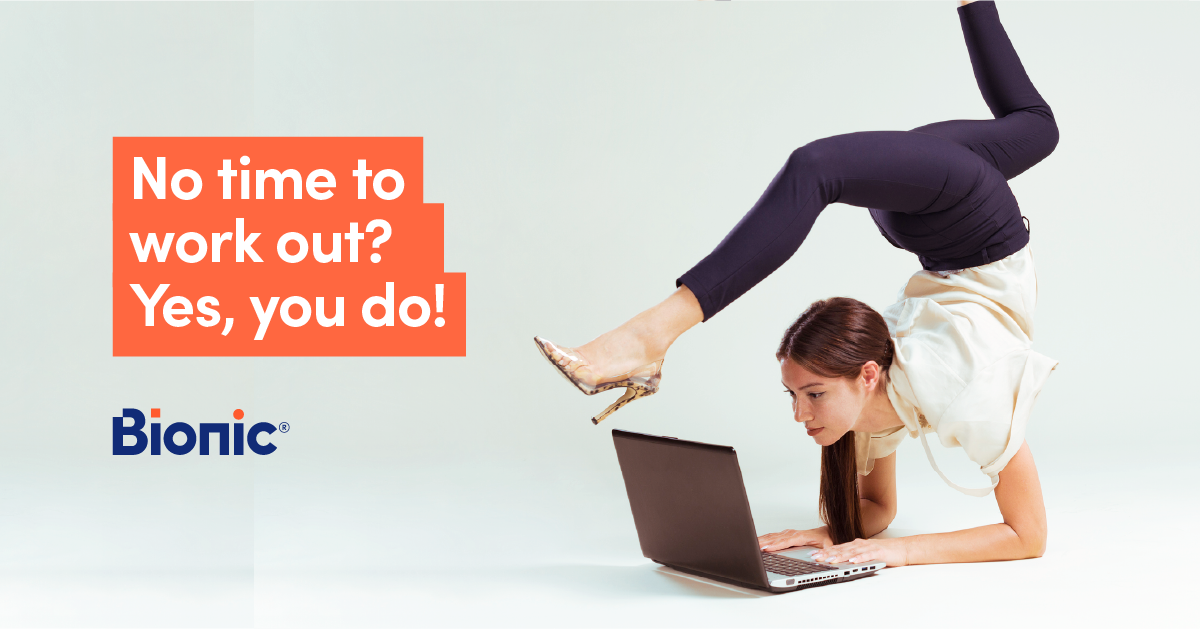 Woman in blue trousers and white shirt works on a laptop while bending her legs over her head