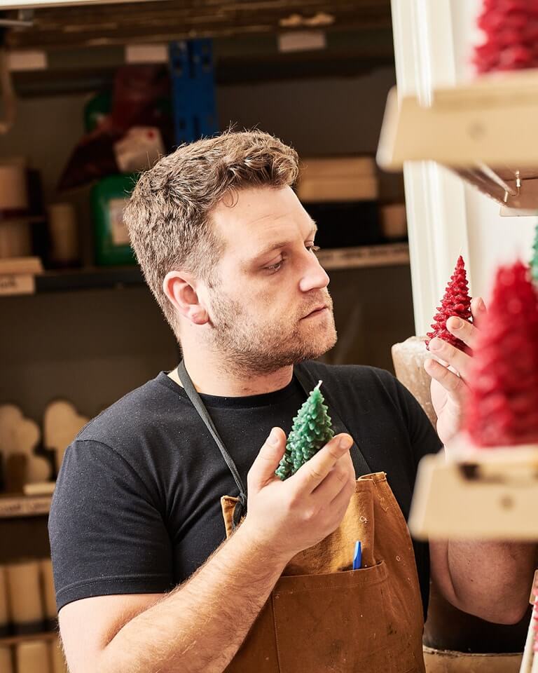 Recycled Candle Company owner Richard examines two red and green Christmas tree candles