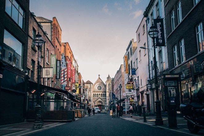 A brightly coloured row of shops either side of a street in Dublin with a church in the distance.