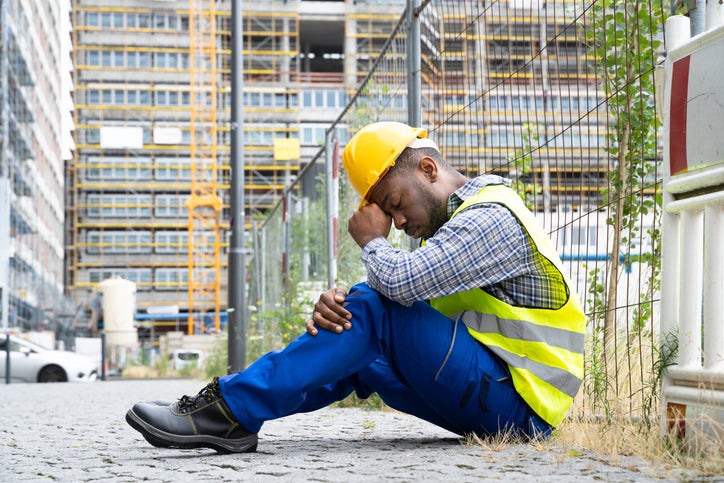 A dejected looking construction worker sits on the floor after being made redundant by the business he worked for
