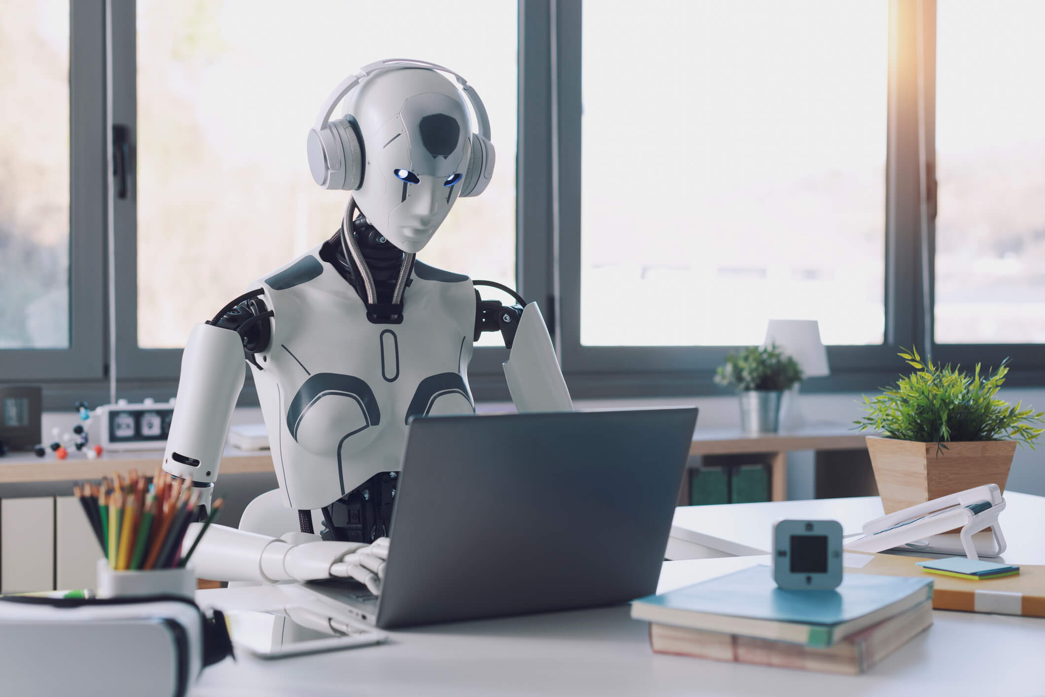 Ai robot sat at an office desk working on a laptop