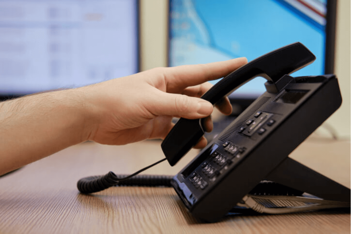someone picking up a desk phone receiver on a desk