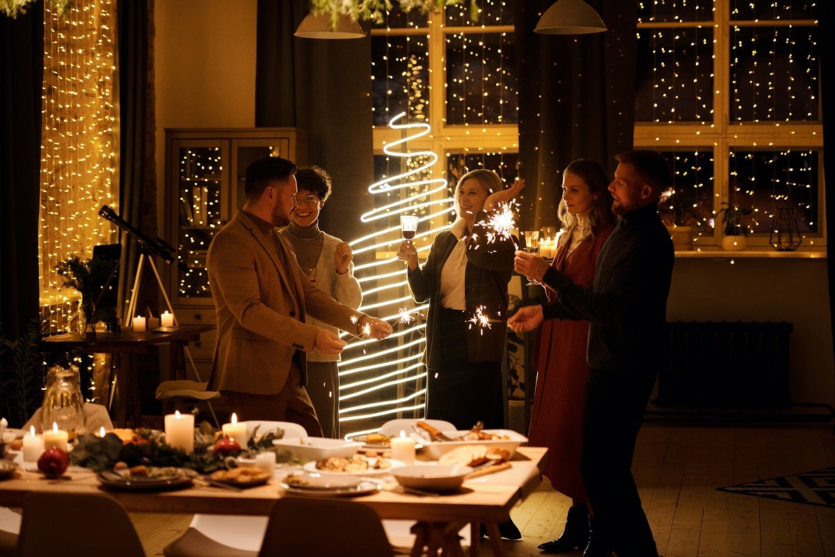 A group of people laughing in front of sparkling fairy lights and a golden Christmas tree