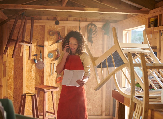 a small business owner recycling furniture from her garden workshop talks on the phone about the workshop insruance documents she is holding