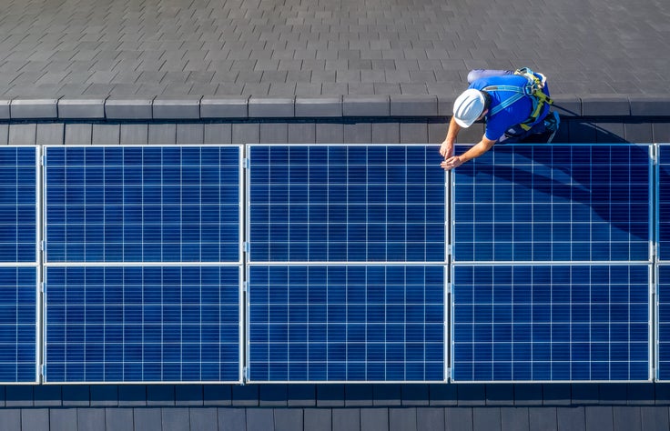 Male engineer in blue suit and protective helmet installing photovoltaic panel system at a business property