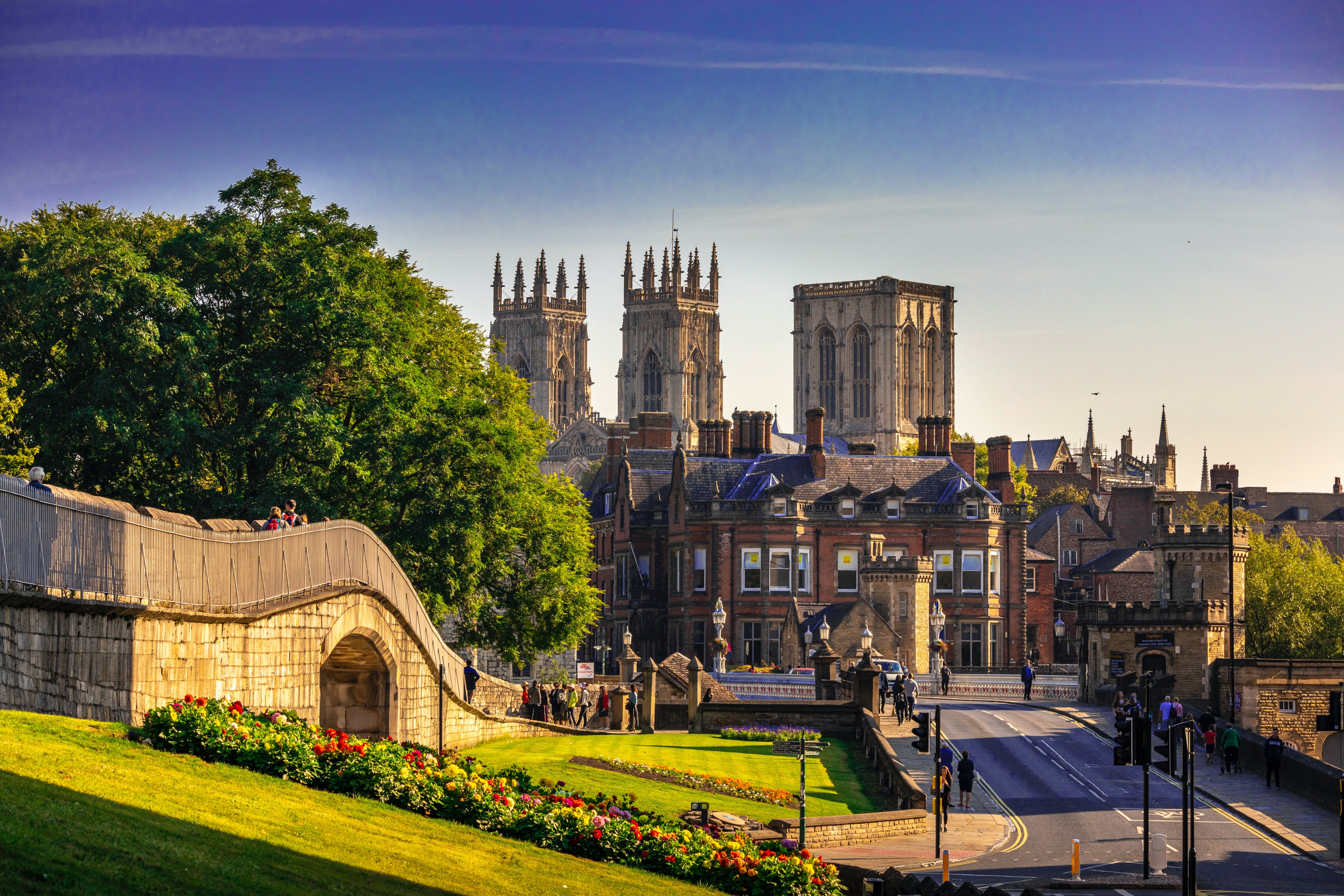 A street in York with an old bridge over the road flanked by green embankments. York Minster catherdral is in the background.