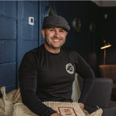 Mark Hepworth of Flat Cap Coffee Roasting Co. sat on bag of coffee beans