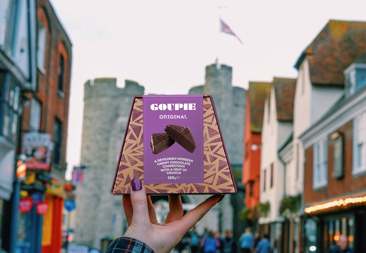 Box of Goupie chocolate being held up on high street in front of a castle.