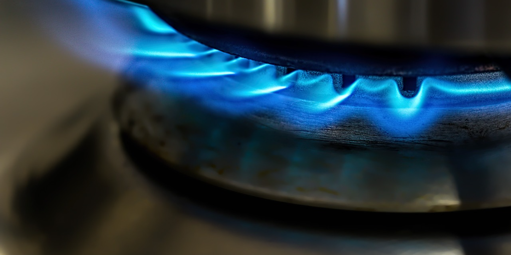 Blue gas flame on silver cooker hob with pan on top.