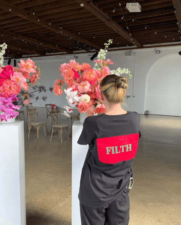 A Filth Florist employee wearing a Filth logo t-shirt sets up a floral display at a wedding venue.