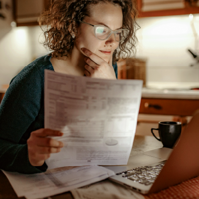 Woman wearing glasses looks at laptop screen while holding unsecured business loan application form