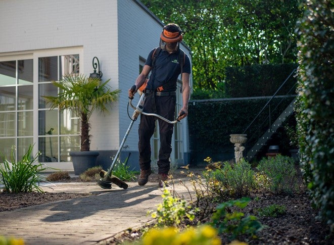 A male gardener in Leeds uses a strimmer to remove grass from edges of a driveway
