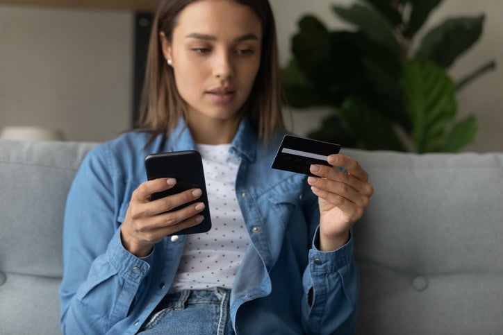 A woman looks nervous as she makes an internet purchase and gives personal data to fraudulent phone scam using her smartphone.