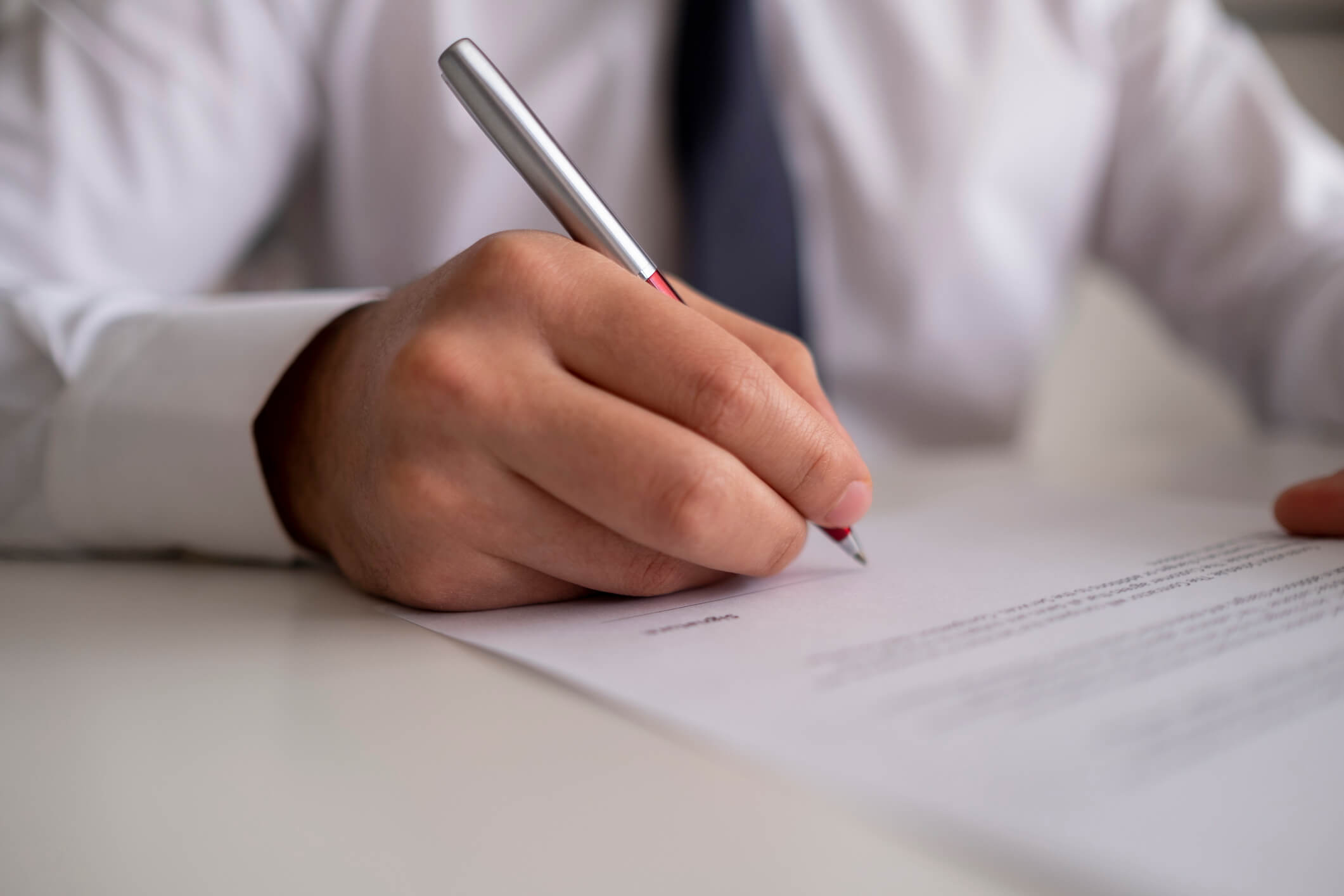 man in a shirt and tie holding a pen and signing a paper agreement