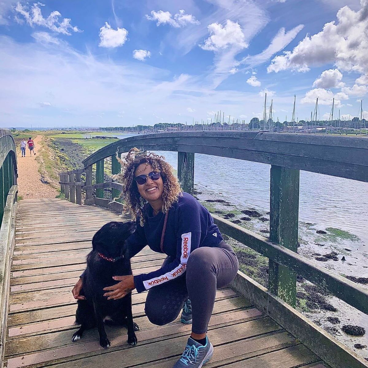 Jessie Stacey, owner of The Animal Days, sits with a dog on a boardwalk next to a river