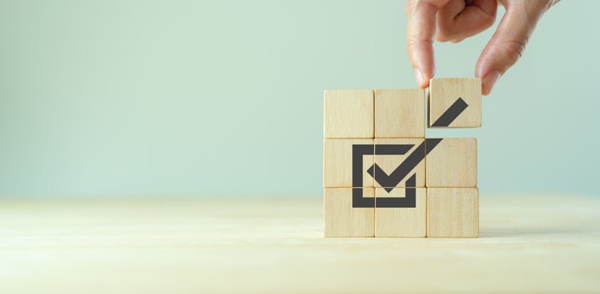 A hand places the final wooden cube of nine to show a Quality and ISO symbol with checkmark icon.