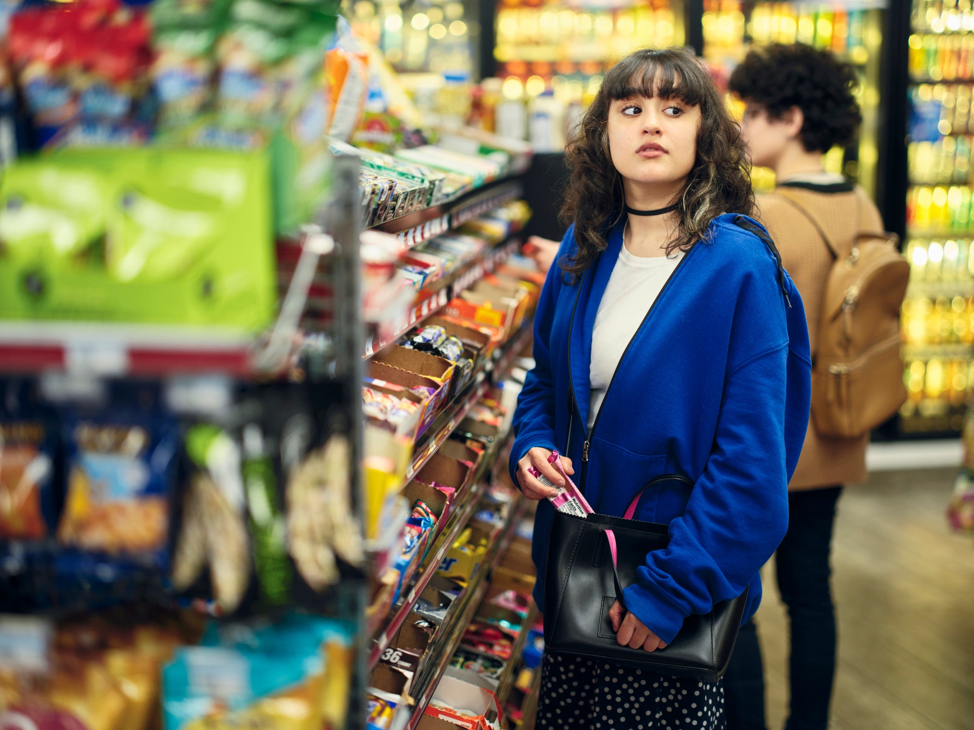 A young woman shoplifting (stealing) merchandise in a convenience store. Shoplifting is sometimes not covered as standard in business insurance policies.