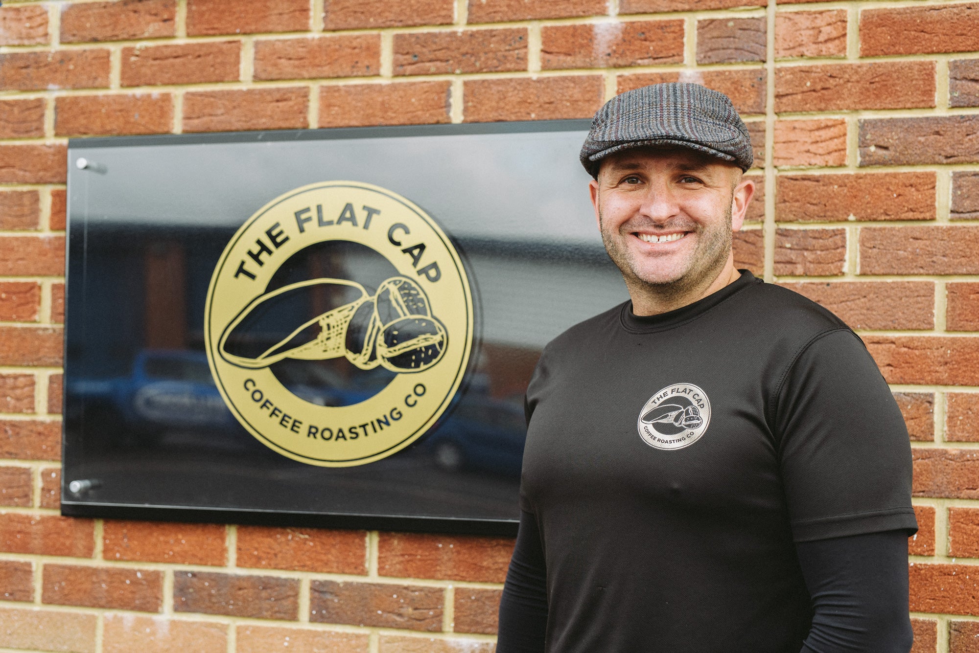Mark Hepworth standing next to wall displaying Flat Cap Coffee Roasting Co. sign