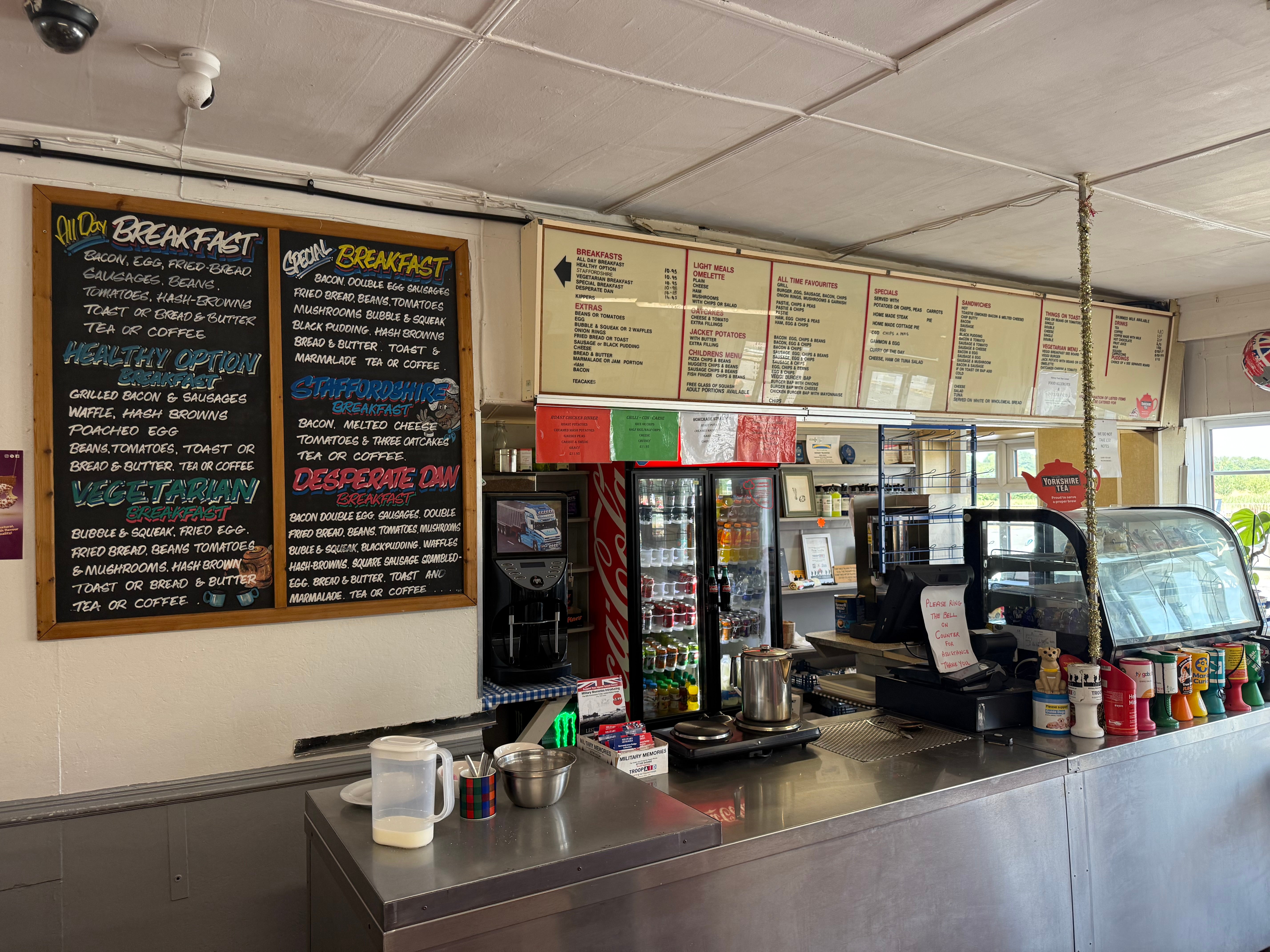 Counter area of the Midway Truckstop with large breakfast menu boards on the wall, a drinks refrigerator, serving counter, and food display case, showing a traditional diner-style interior.
