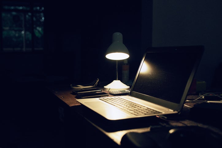 A battery powered desktop lamp lights up a desk and laptop during a blackout power cut