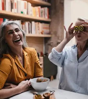 Zwei ältere Frauen sitzen an einem Tisch und lachen.