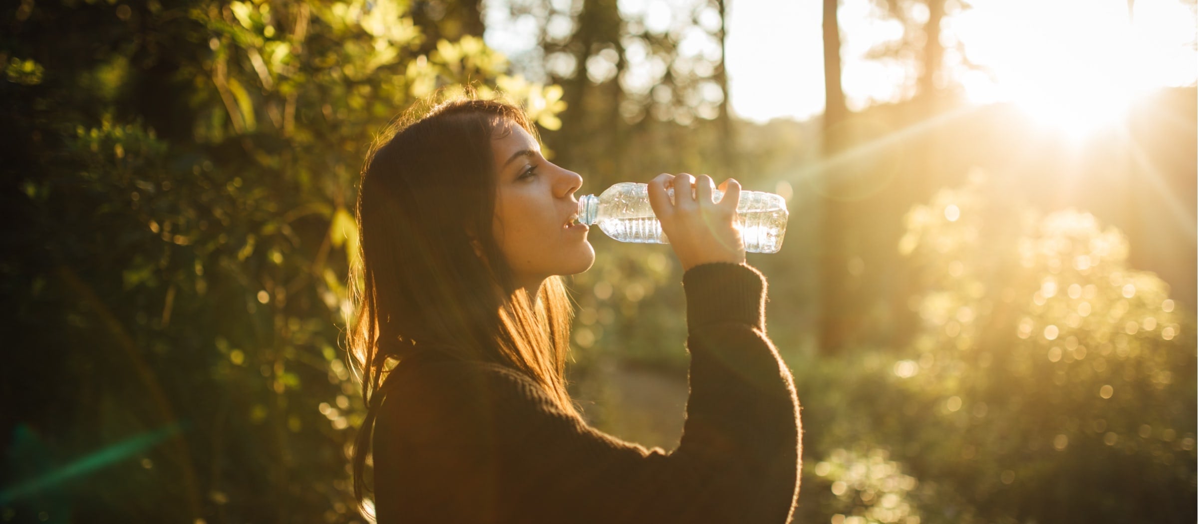 Junge Frau, die in der Natur aus einer Wasserflasche trinkt.
