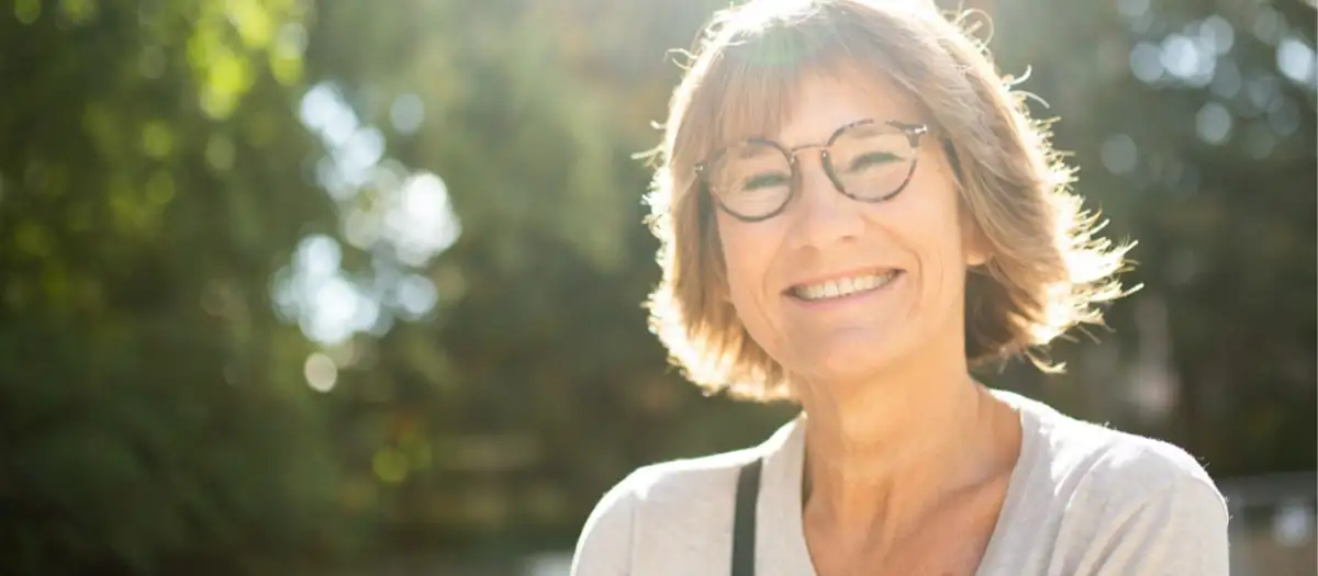 Eine Frau lächelt glücklich, im Hintergrund Bäume.
