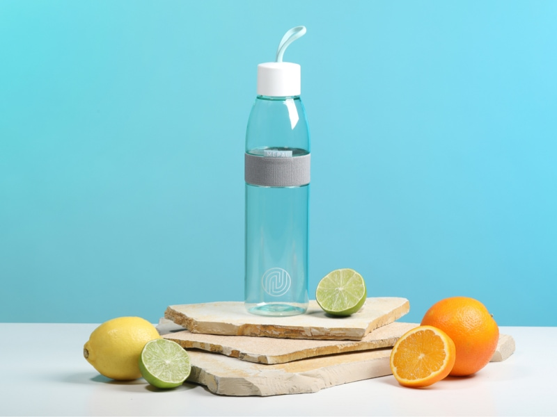 Mepal Flasche mit ENTDECKE DEIN NEO-Logo steht auf Steinplatten, daneben Obst.