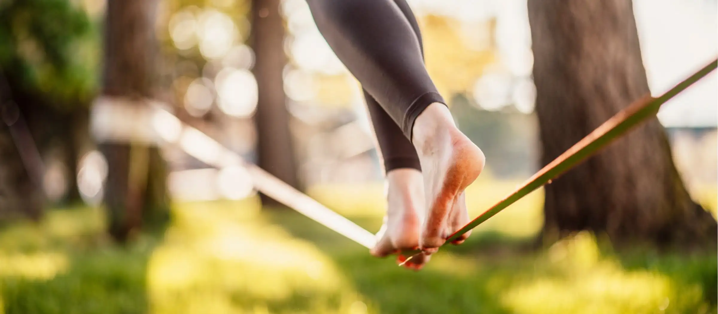 Frau läuft über eine Slackline, die zwischen zwei Bäumen gespannt ist.