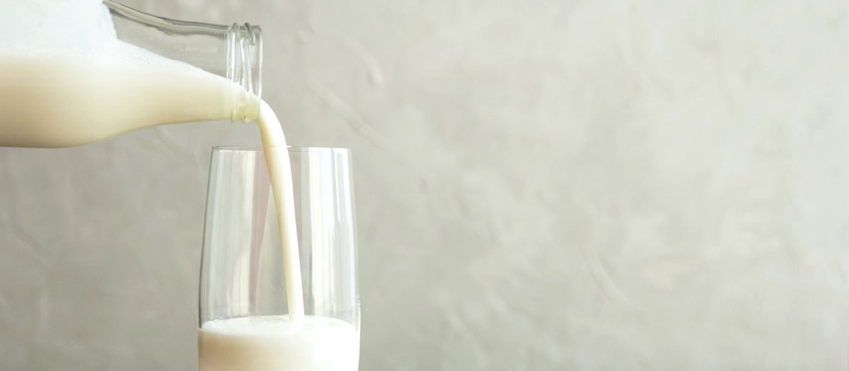 Milch aus einer Flasche wird in ein Glas eingeschenkt.