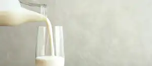 Milch aus einer Flasche wird in ein Glas eingeschenkt.